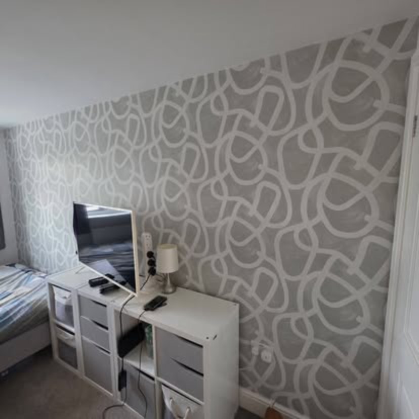 A bedroom feature wall in a looping grey and white patterned paper, running up to a sloped ceiling