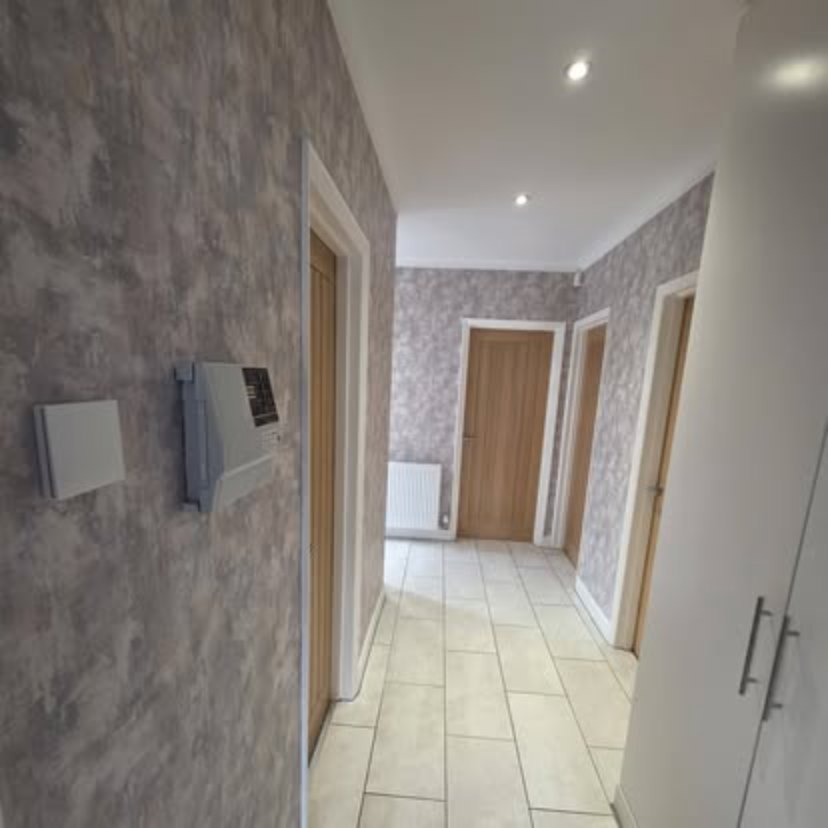 A hallway papered in grey, with white painted door frames, oak doors and a tiled floor running away from the camera