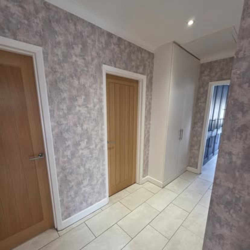 A hallway papered in mottled grey, with two oak doors in white painted frames and a cream tiled floor