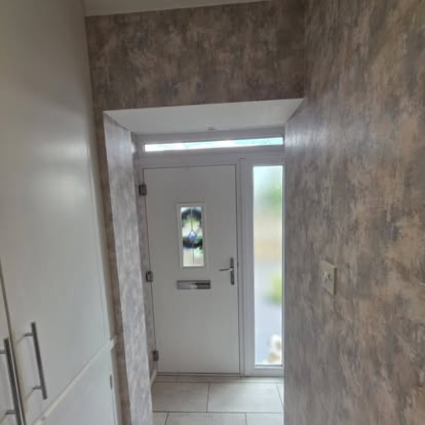 An entrance porch papered in a grey concrete effect, looking out through a white front door with a leaded glass panel