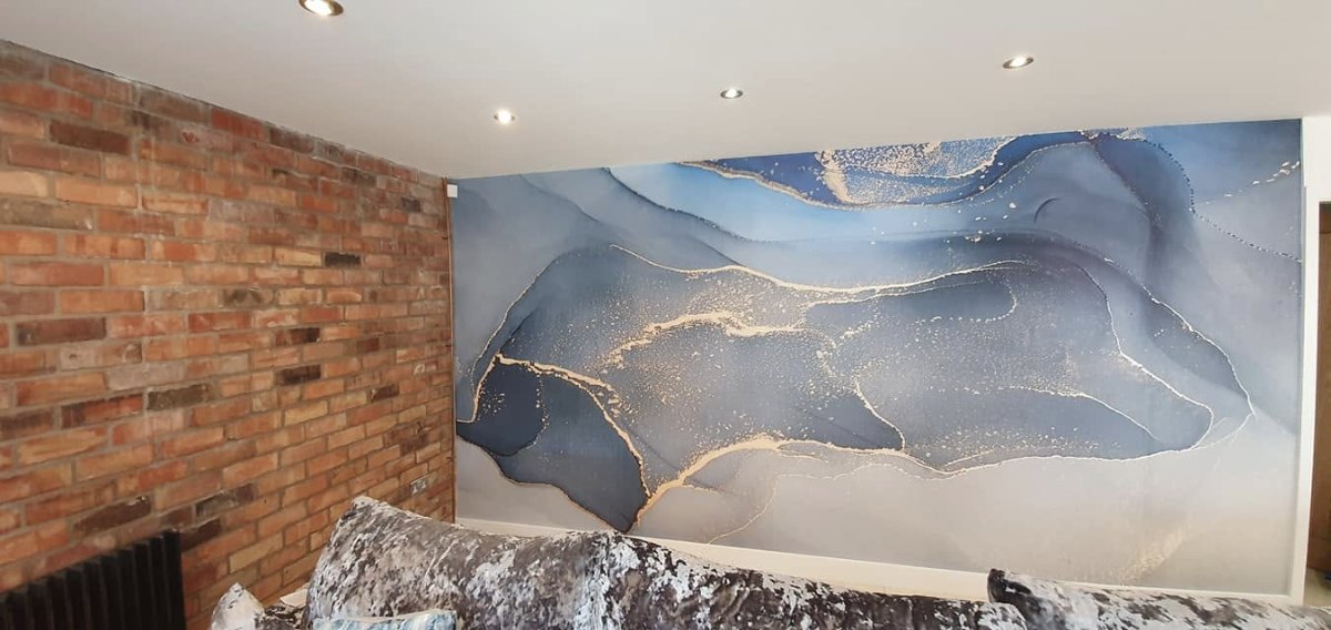 A hung wall mural in blue and gold beside an exposed red brick wall, lit by ceiling spotlights