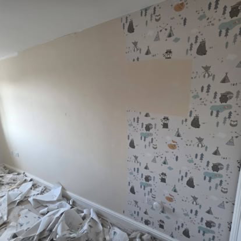 A child's bedroom part way through stripping, with patterned paper half removed, bare wall showing and stripped paper piled on the floor